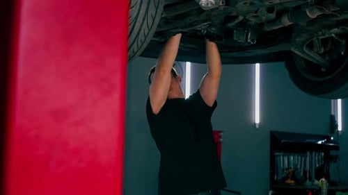 an Auto Mechanic at Service Station Checks a Car Being Lifted on a Lift Fixing Problems with a