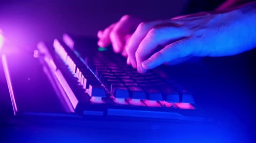 Man is Typing Intently on a Keyboard with Purple and Blue Lights Illuminating the Room