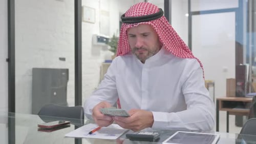 Man Counting Money in Office with Calculator