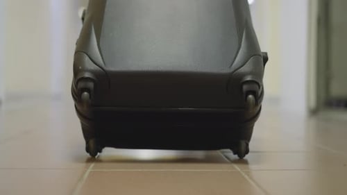 Pequenas rodas de uma grande mala preta giram no chão de cerâmica
