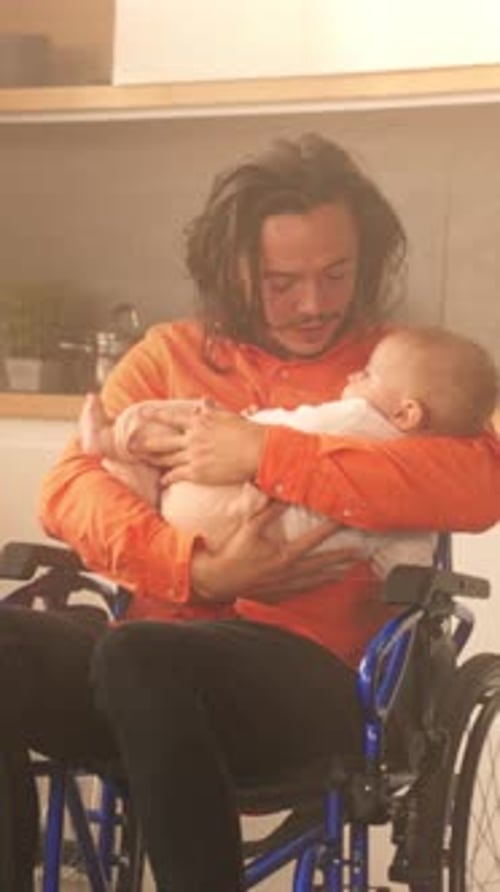 Adult Holds Infant While Seated in Wheelchair Indoors