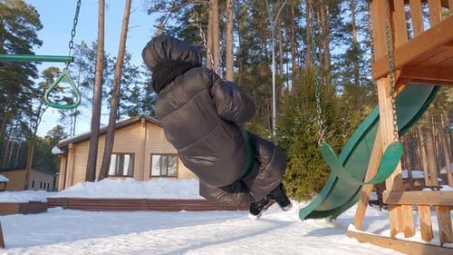 Blondy Happy Teen Girl in Down Jacket is Swinging on Swings in Winter Park