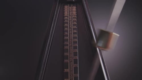 An old fashioned metronome swings back and forth in front of a gray background