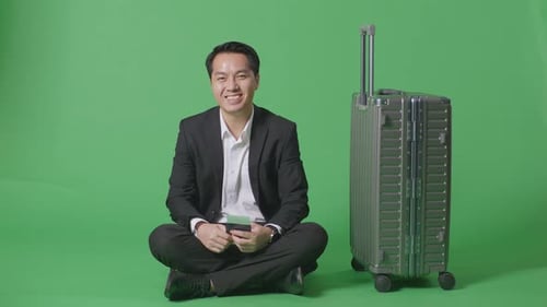 Businessman With Luggage Holding Passport And Smiling To Camera While Sitting In The Green Screen