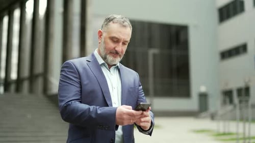 Successful senior investor with mobile phone outside office building Middle-aged businessman