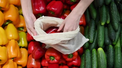 Mujer recogiendo pimientos en una bolsa reutilizable en una tienda. Temáticas del Día de la Tierra y la Ecología. Cámara lenta