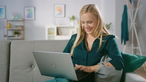 Smiling woman using laptop sitting on couch at home