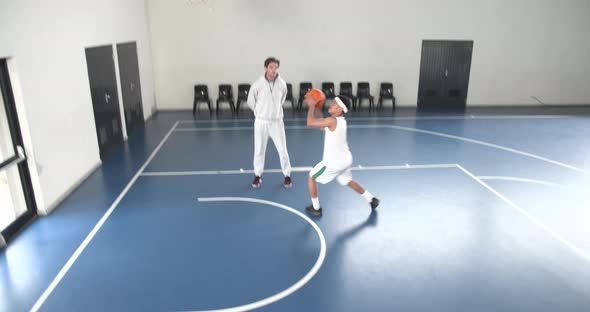 Coach observing basketball player practicing dribbling skills on indoor ...