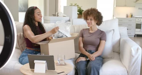 Des femmes afro-américaines déballant un nouveau colis sur un canapé, déchirant un film à bulles, révélateur, appareil pour vlog