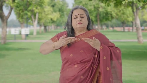 Relaxed Indian old woman doing breathe in breathe out exercise in park