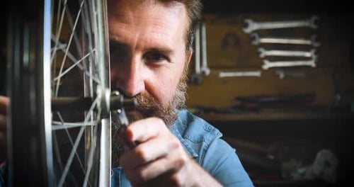 Well-groomed handsome bearded master hipster, specialist in bicycles, repairing a bicycle in his w