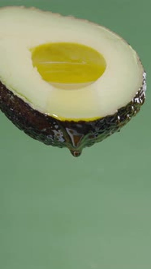 Oil is dripping down from cut in half avocado fruit.