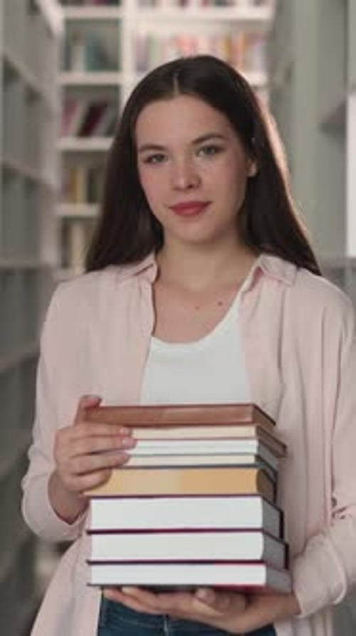 Young Teacher with Folio Stack in Library
