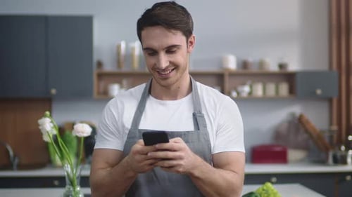 Smiling Man Browsing Phone in Kitchen