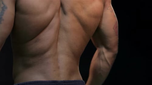 Muscular Man Kneads His Back Muscles Against a Striking Black Backdrop