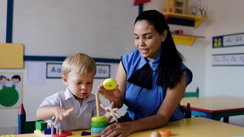 Teacher helping kid with wooden toy at kindergarten school class. Education, smart games children