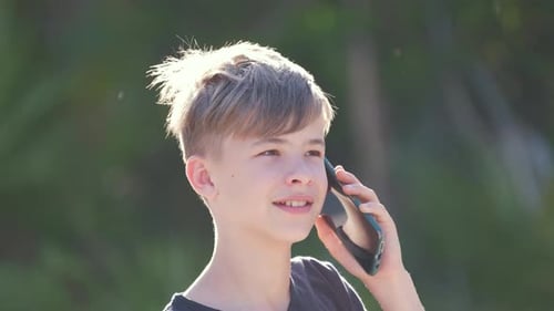 Happy Young Boy Talking on Cellphone Outdoors in Summer Park