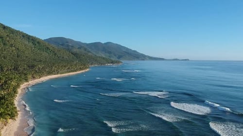Drohne, die sich sanft entfernt, um wunderschöne Berghänge, weißen Sandstrand und Meereswellen zu entdecken