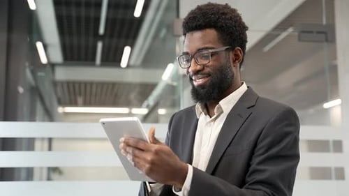 Happy confident african american businessman is using digital tabletstanding in business office. Man