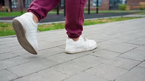 Close Leg View of Woman in Maroon Joggers and White Sneakers on Tiled Pavement