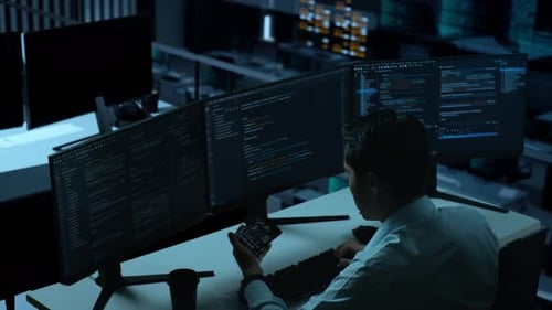 Happy Asian Man Looking At Code On Mobile Phone While Write Code With Multiple Screens In office