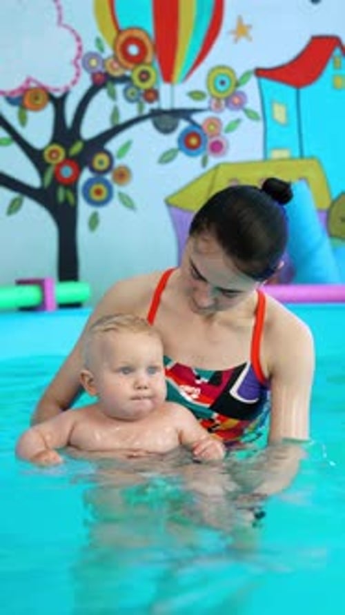 Brünette kaukasische Frau im Badeanzug mit einem Kind im Schwimmbad.