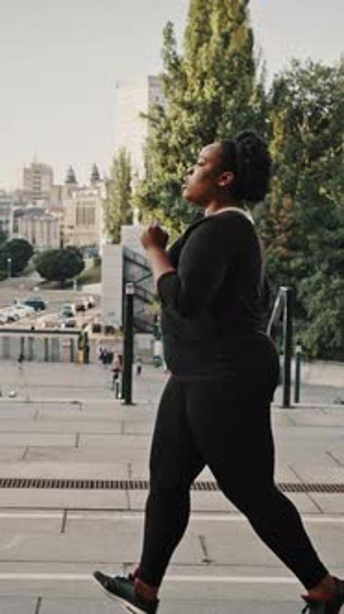 Side View Portrait of Young Overweight African American Woman Jogging Alone in Urban Park Practicing