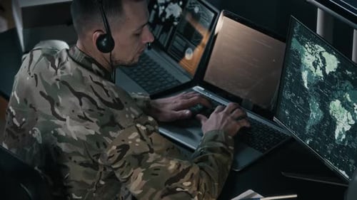 Man in Camouflage Working on Computers with World Map