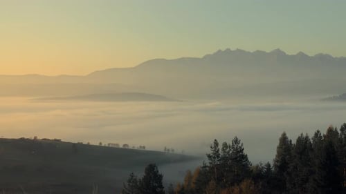 Big rocky mountain peaks in the background with a mist covering the valley and small hills in the fo