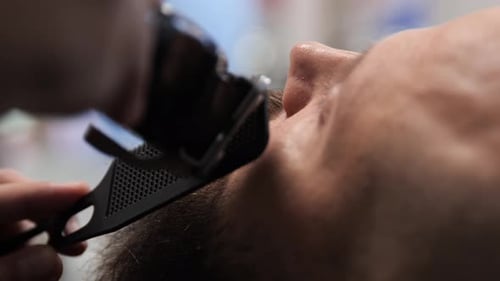 Close up of a moustache being trimmed and combed by a barber. Young attractive bald man with long da