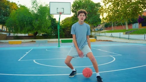 Teen Boy Dribbling Basketball on Blue Court