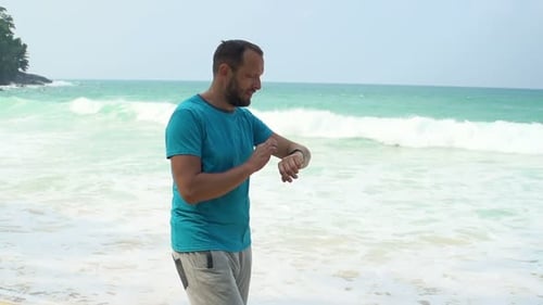 Young man checks pulse on smartwatch during beach workout in super slow motion