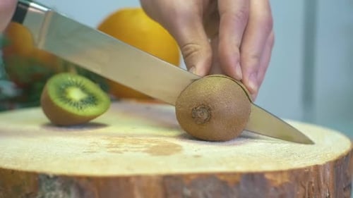Slow motion girl Hand Slicing Kiwi Sharp Knife Slicing Fresh Kiwi fruit Close Up on wooden cutting b