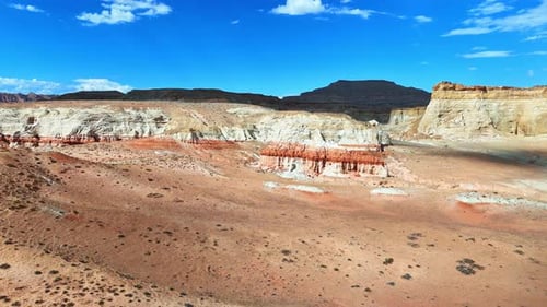 Flying over the barren desert lit by the bright hot sun. Approaching bare rocks under blue sky