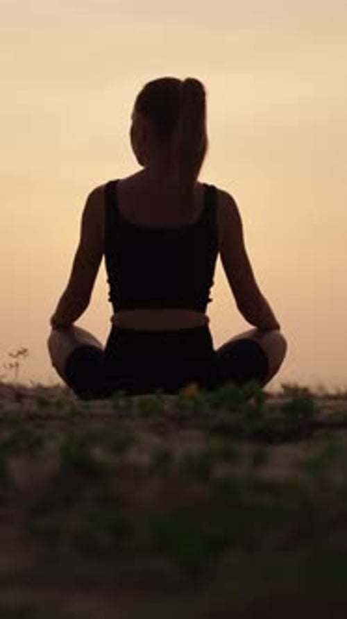 Méditation dans la nature tôt le matin, vue arrière d'une femme assise en position du lotus, vidéo verticale