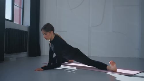 Junge erwachsene Frau streckt im Yoga-Studio die Beine und praktiziert traditionelle Asana in geteilter Position