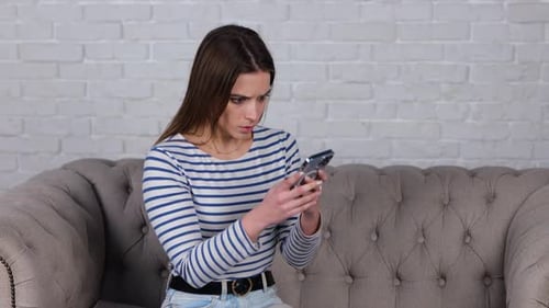 Woman Using Smartphone Looking Worried on Couch