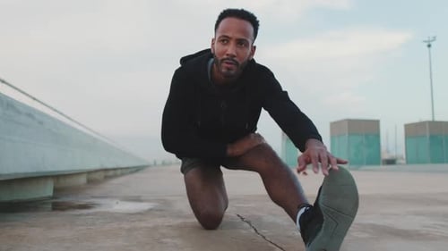 Young athlete doing warm-up, leg stretching before training on the embankment