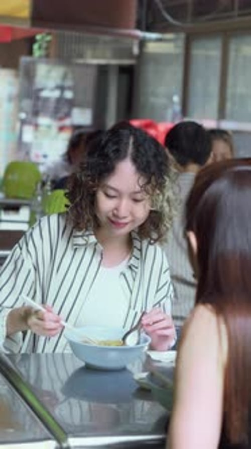 Two women eating noodles together at a casual outdoor restaurant