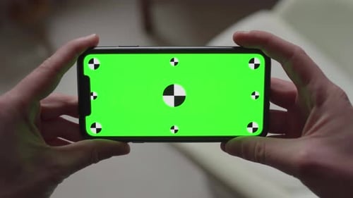 two hands holding smartphone with green screen display and tracking markers, changing orientation fr