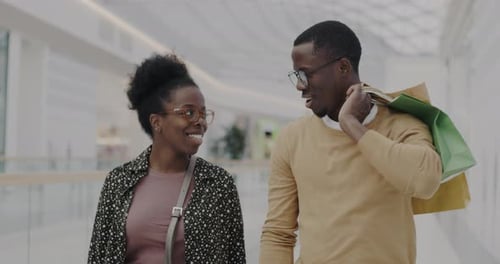 Man and Woman Happy Couple Walking in Shopping Mall Carrying Bags Talking Smiling Hugging