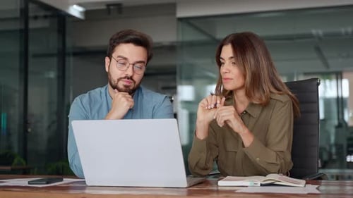 Two Busy Colleagues Working Together Talking Using Laptop in Office
