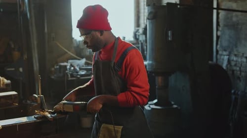 Afroamerikanischer Schmied macht Metallarbeiten mit Winkelschleifer in der Werkstatt