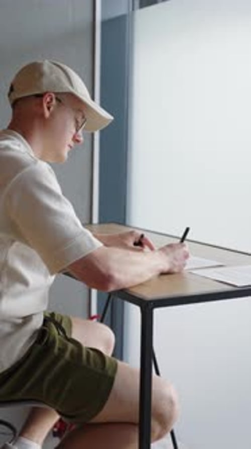 Vertical - l'homme est assis près du bureau et écrit sur du papier, lumière vive provenant de la fenêtre