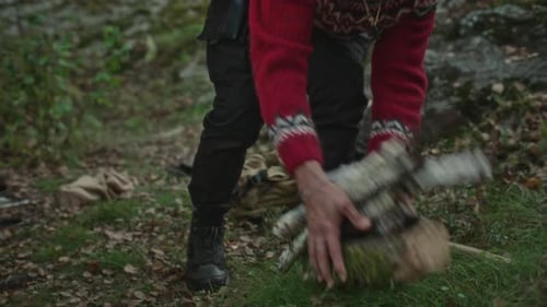 Man Bringing Bundle of Chopped Firewood and Axe to Forest Campsite