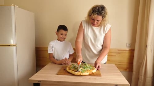 Woman Cuts Pizza Next to Child in Kitchen