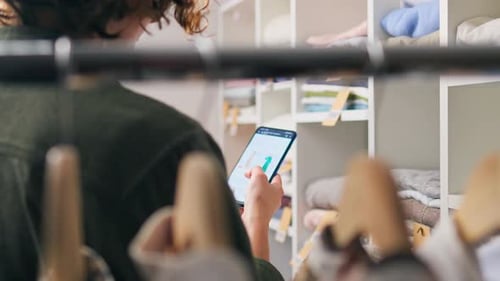 Woman Browsing Clothing on Mobile Phone in Store