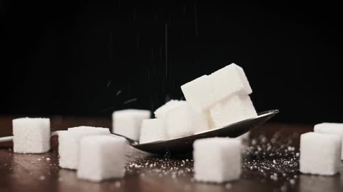 Ein Stapel von Zuckerwürfeln im Löffel wird auf dem Tisch auf schwarzem Hintergrund gedreht. Nahaufnahme
