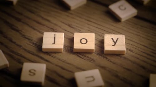 Camera Pans Across Wooden Tiles Spelling Joy on Rustic Wooden Table