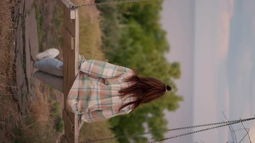 Vidéo verticale Une brune vêtue d'une chemise à carreaux se balance sur une balançoire en bois à l'extérieur de la ville sur le